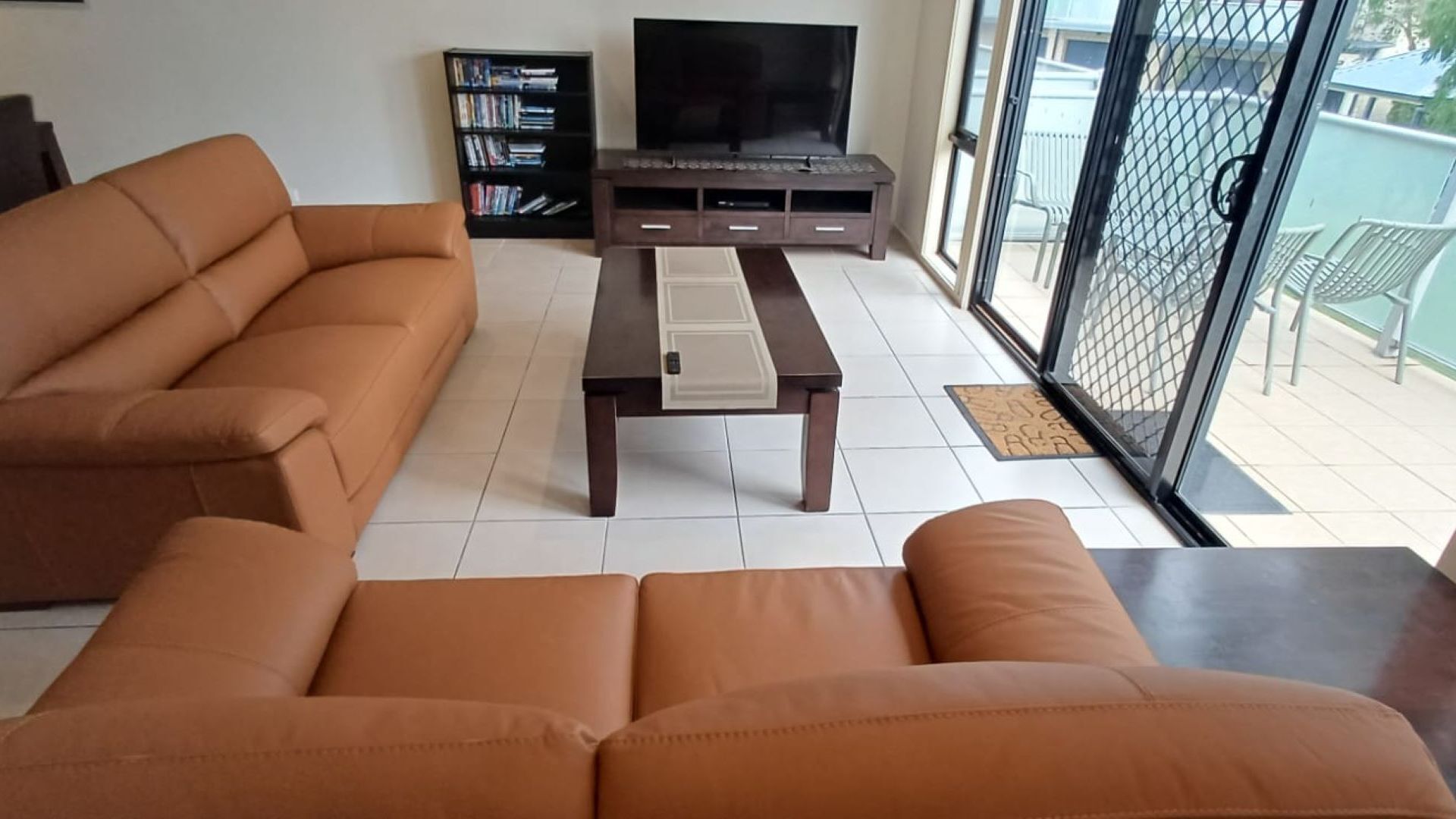 A living room with a sofa, a coffee table, a TV stand with a flat-screen TV, and a bookshelf.