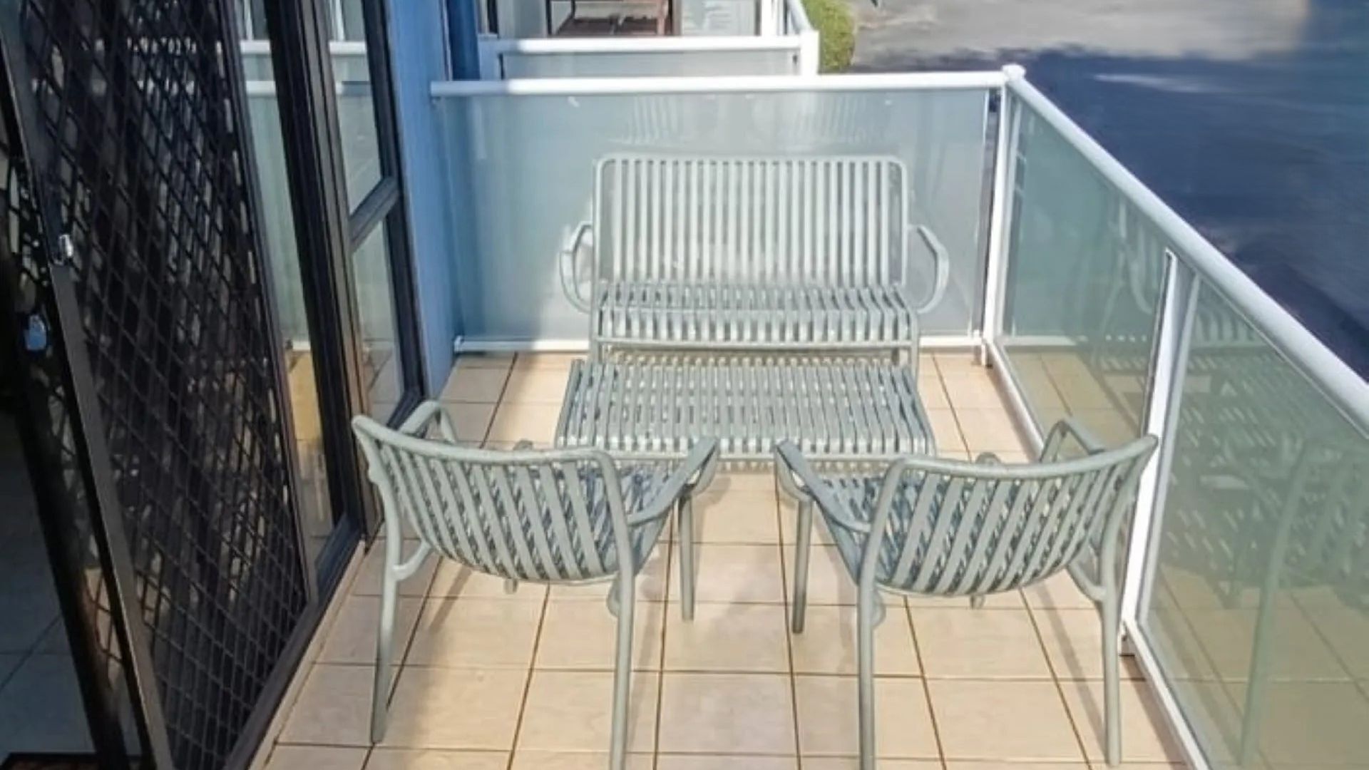 A balcony with two metal chairs and a small table, a glass railing, and a view of the sea.