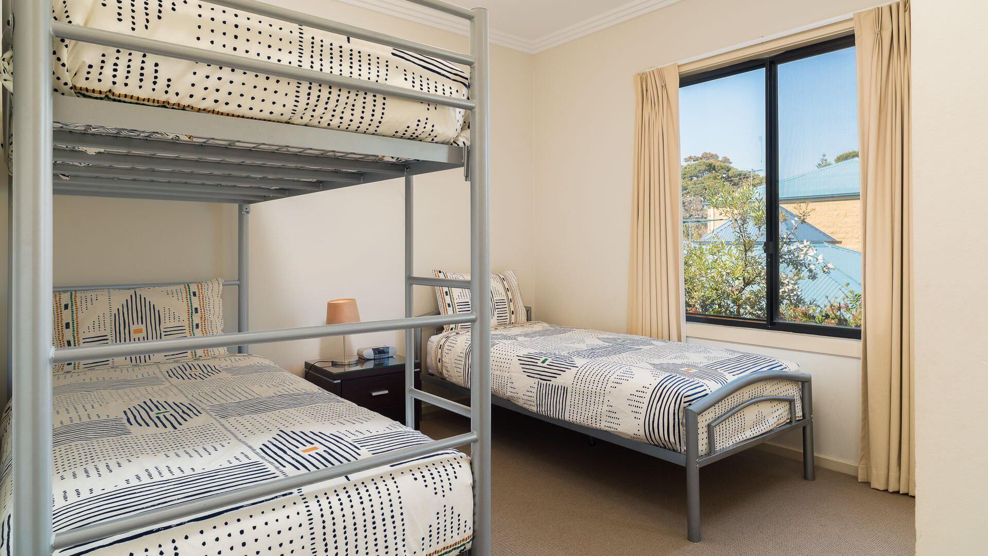 Une chambre avec des lits superposés, une fenêtre avec des rideaux et une vue sur un bâtiment à l’extérieur.