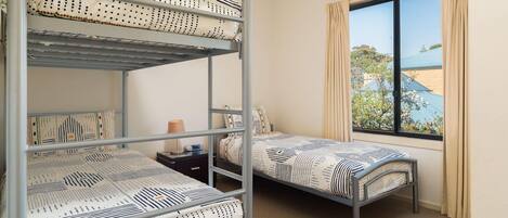 Une chambre avec des lits superposés, une fenêtre avec des rideaux et une vue sur un bâtiment à l’extérieur.