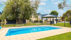 A swimming pool with a tiled deck, surrounded by a fence, and a covered pavilion. - Penguins by the Beach - sleeps 9 (COWES)
