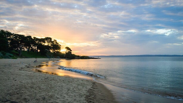 A beach with calm waters, trees, and a sunset. - Penguins by the Beach - sleeps 9 (COWES)