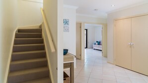 A staircase leading to a landing with a bowl on a small table, a door, and a hallway with a sofa and a tiled floor. - Penguins by the Beach - sleeps 9 (COWES)