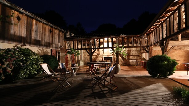 An outdoor wooden deck with seating and a table, surrounded by rustic buildings and greenery. - Mansion - RIMBEZ ET BAUDIETS (Rimbez-et-Baudiets)