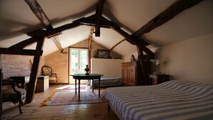 A room with a sloped ceiling, wooden beams, a bed with a striped bedspread, a table with a patterned rug, a chair, and a cabinet. - Mansion - RIMBEZ ET BAUDIETS (Rimbez-et-Baudiets)