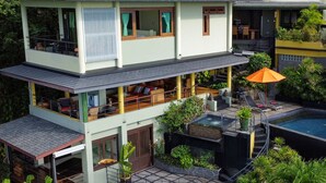 A two-story building with a rooftop pool, outdoor seating, and lush greenery.