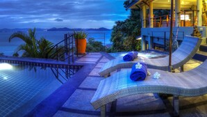 A poolside area with lounge chairs, a hot tub, and a view of the sea.