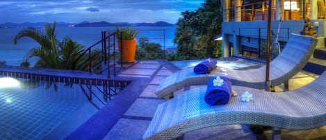 A poolside area with lounge chairs, a hot tub, and a view of the sea.