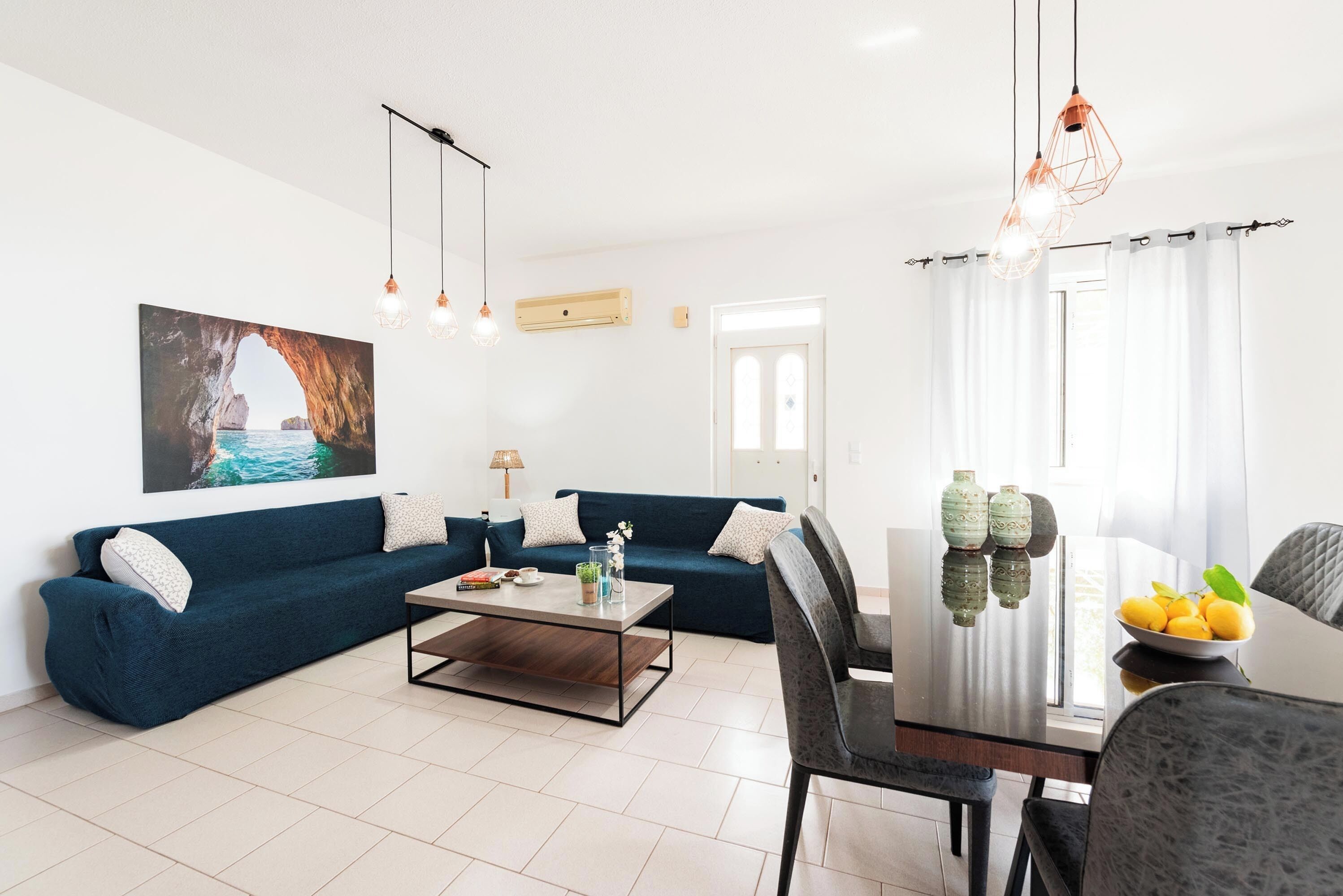 A modern living room with a blue sofa, a coffee table, and a dining area with a table and chairs.