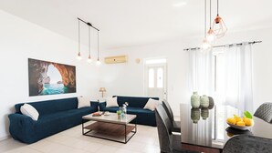 A modern living room with a blue sofa, a coffee table, and a dining area with a table and chairs. - Villa Perla with Sea View (rhodes)
