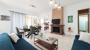 A modern living room with a sofa, coffee table, fireplace, dining area, and kitchen in the background. - Villa Perla with Sea View (rhodes)