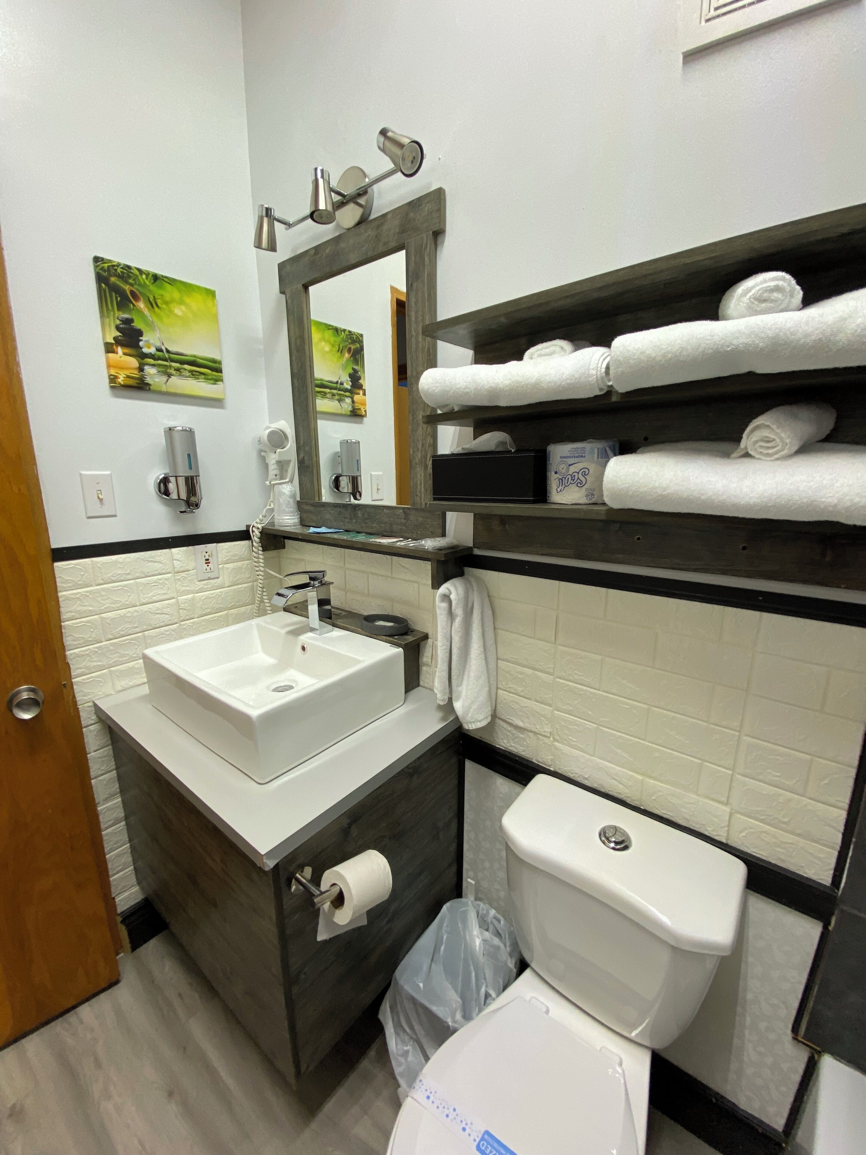 A modern bathroom with a white sink, a toilet, a mirror, and a shelf with towels.