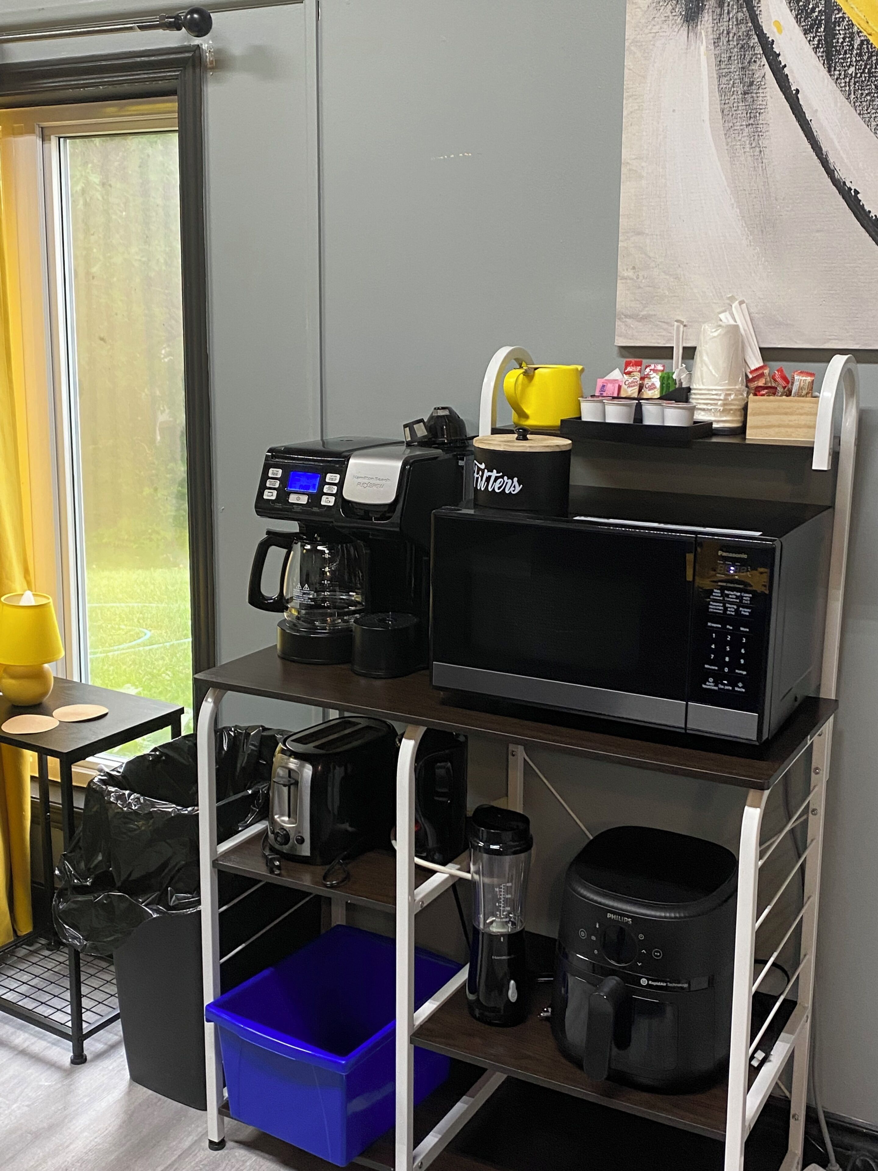 A kitchenette with a coffee maker, microwave, toaster, and storage containers.