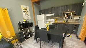 Una cocina compacta con electrodomésticos modernos, un comedor con mesa y sillas, y una pequeña zona de estar con un sofá y una lámpara.