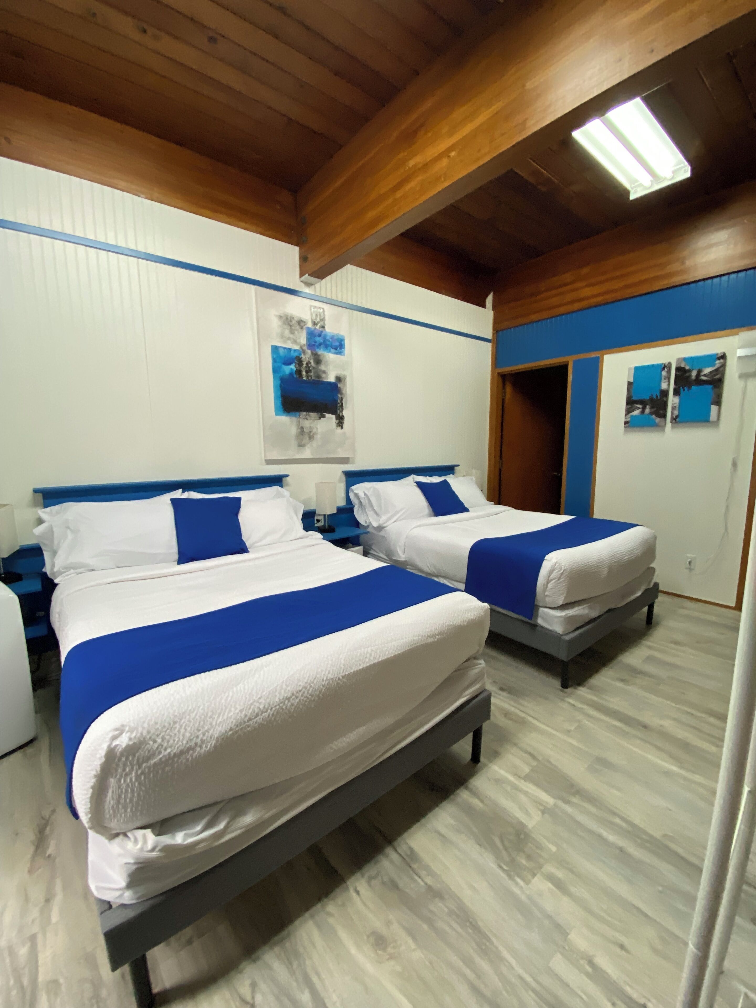 Habitación de hotel con dos camas, vigas de madera en el techo, decoración azul y blanca y suelo de madera.
