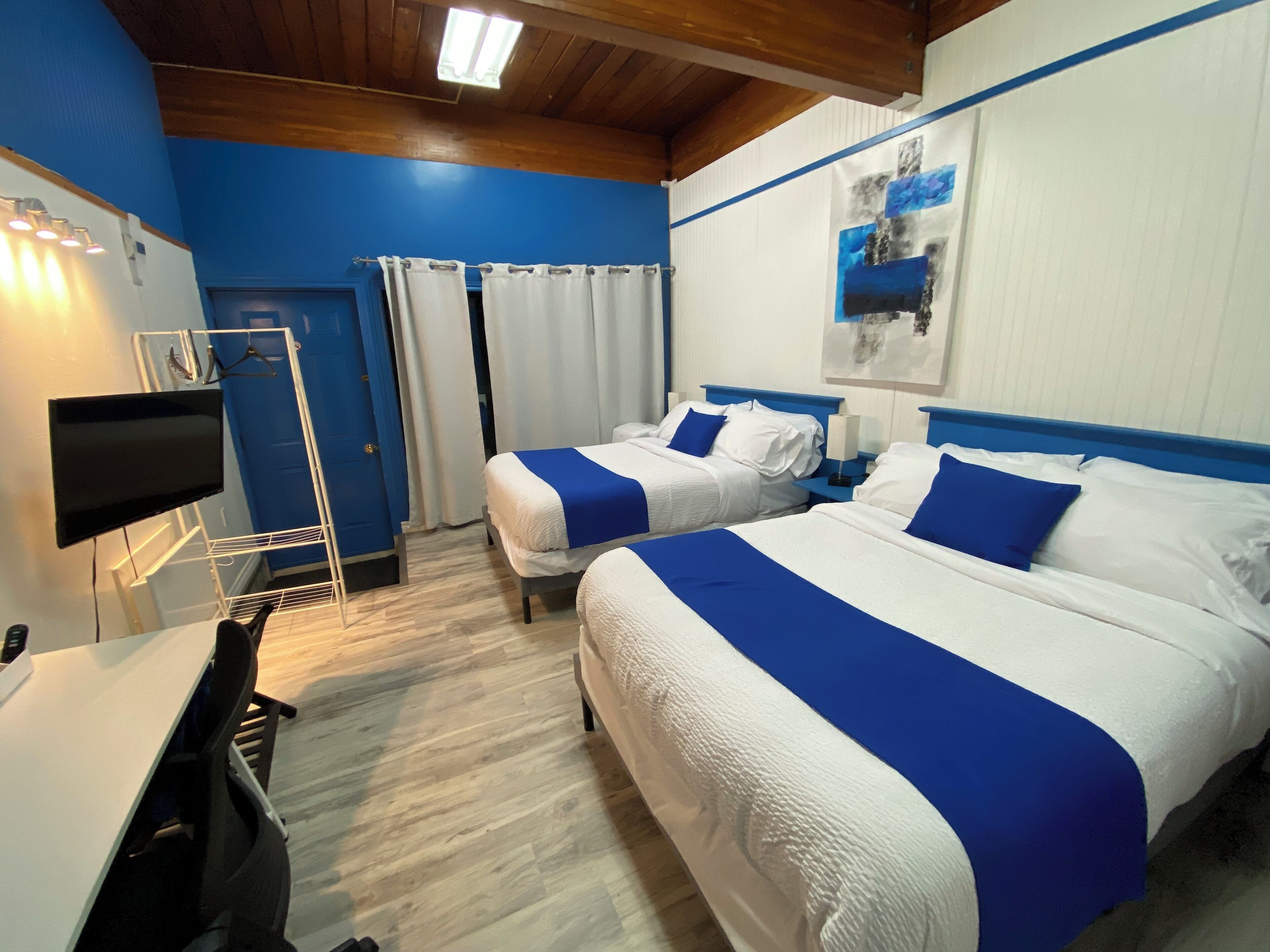 A hotel room with two beds, a TV, a desk, and a shower area.