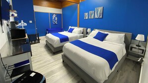 Habitación de hotel con dos camas, un escritorio y una silla. Hay obras de arte en la pared y una lámpara en la mesita de noche.