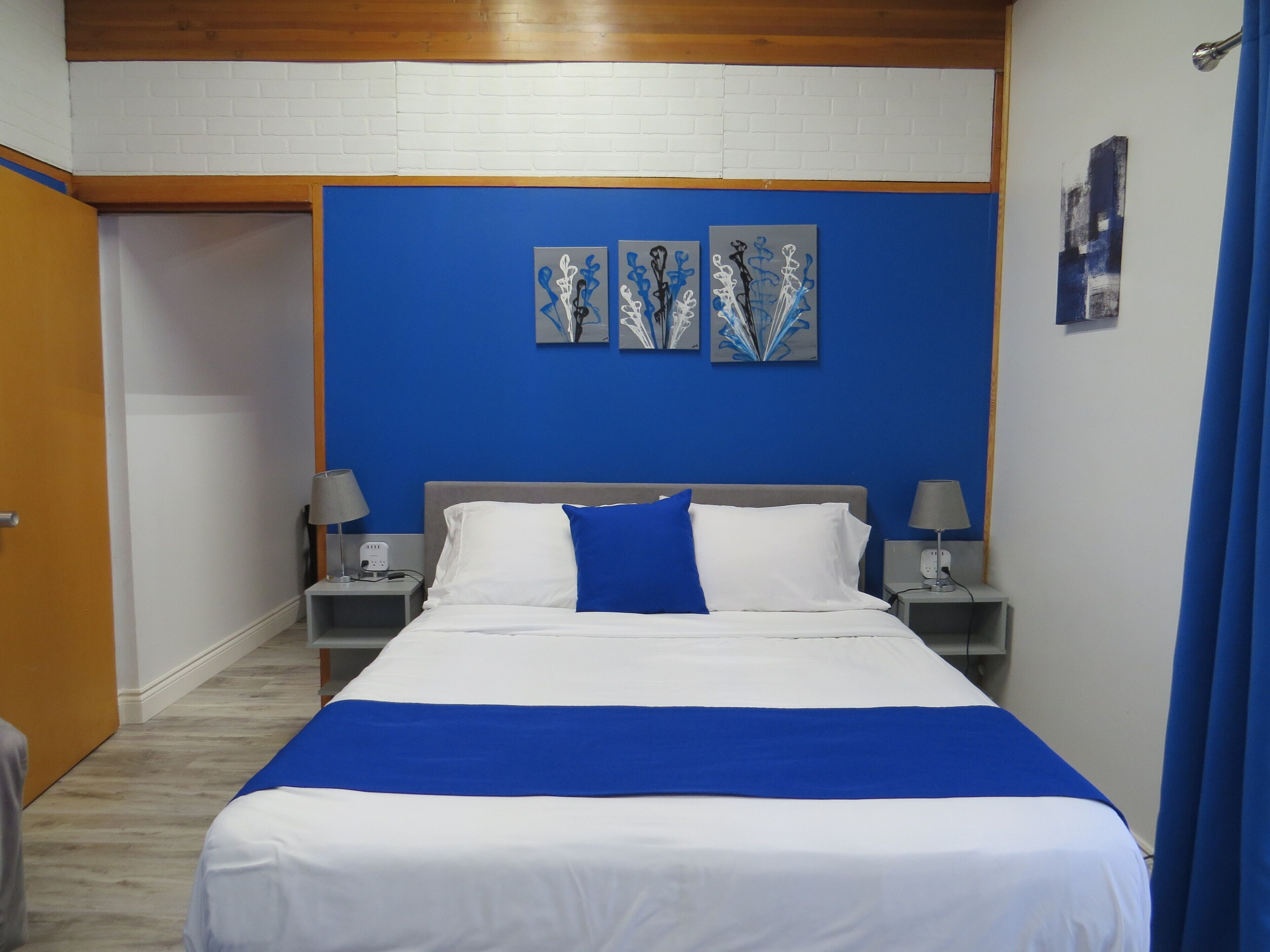 Une chambre d’hôtel avec un lit, deux tables de chevet, un mur bleu et une œuvre d’art au-dessus du lit.
