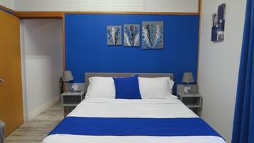 Une chambre d’hôtel avec un lit, deux tables de chevet, un mur bleu et une œuvre d’art au-dessus du lit.