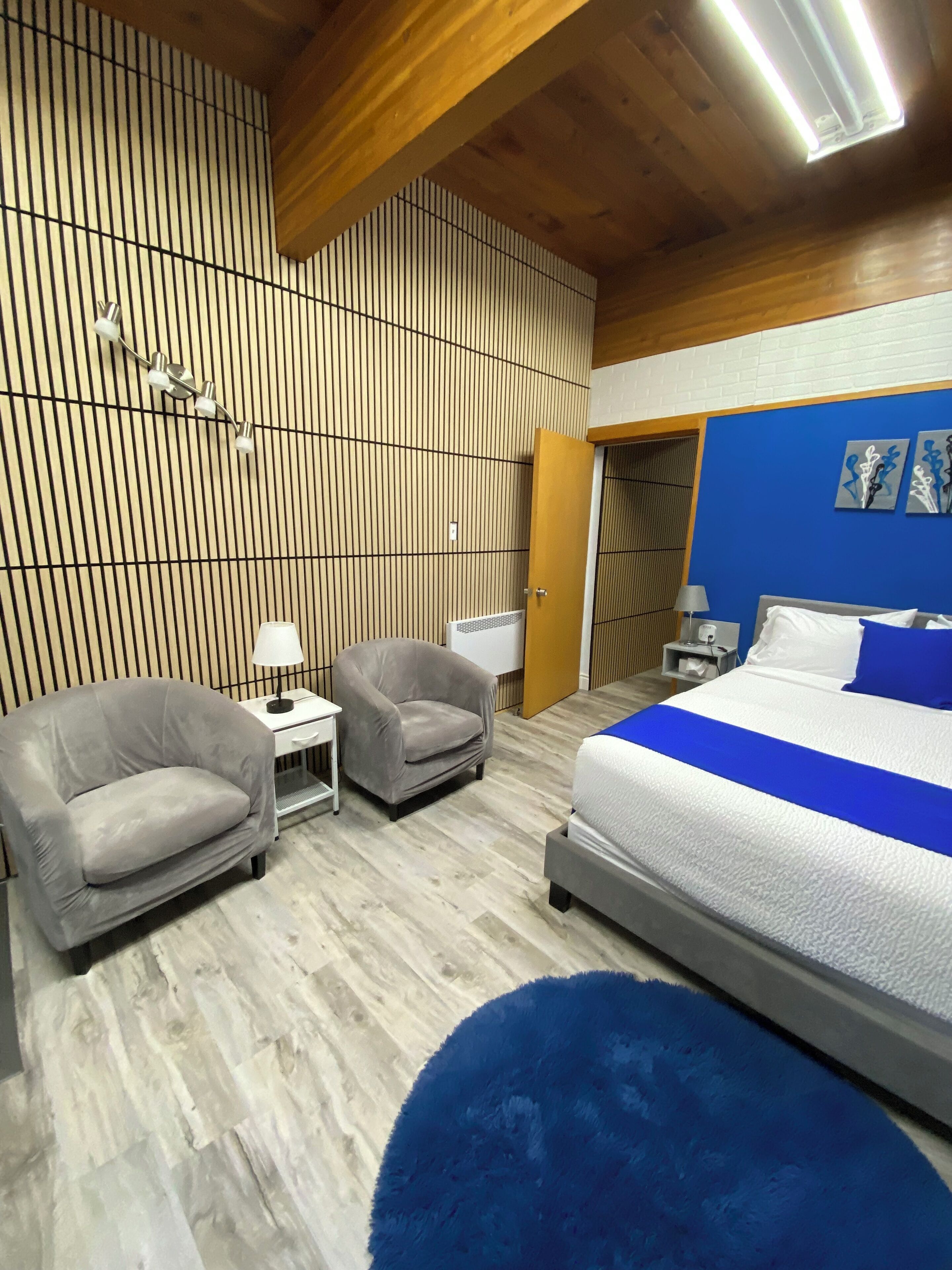 A modern bedroom with a large bed, two armchairs, a small table, and a blue rug.