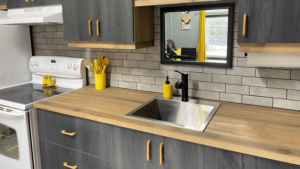 Una cocina moderna con armarios grises, una encimera de madera, un fregadero de acero inoxidable y un horno empotrado.