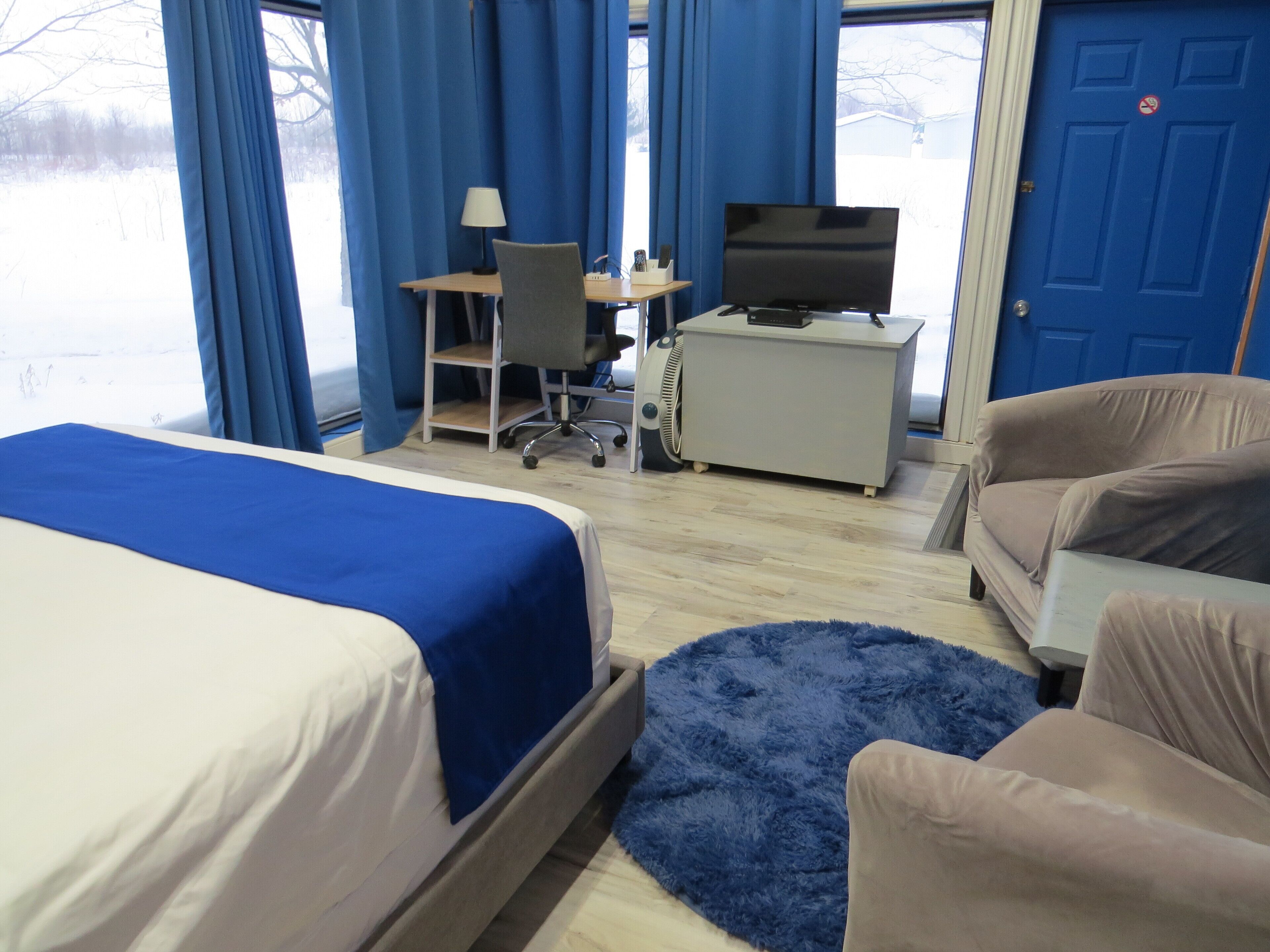 A hotel room with a bed, a desk with a computer and a TV, a chair, and a sofa.