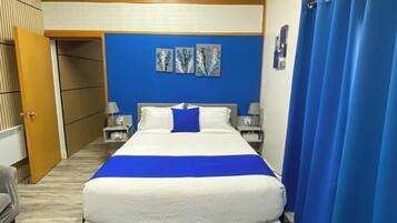 A bedroom with a bed, a blue rug, a wooden ceiling, and a blue curtain.