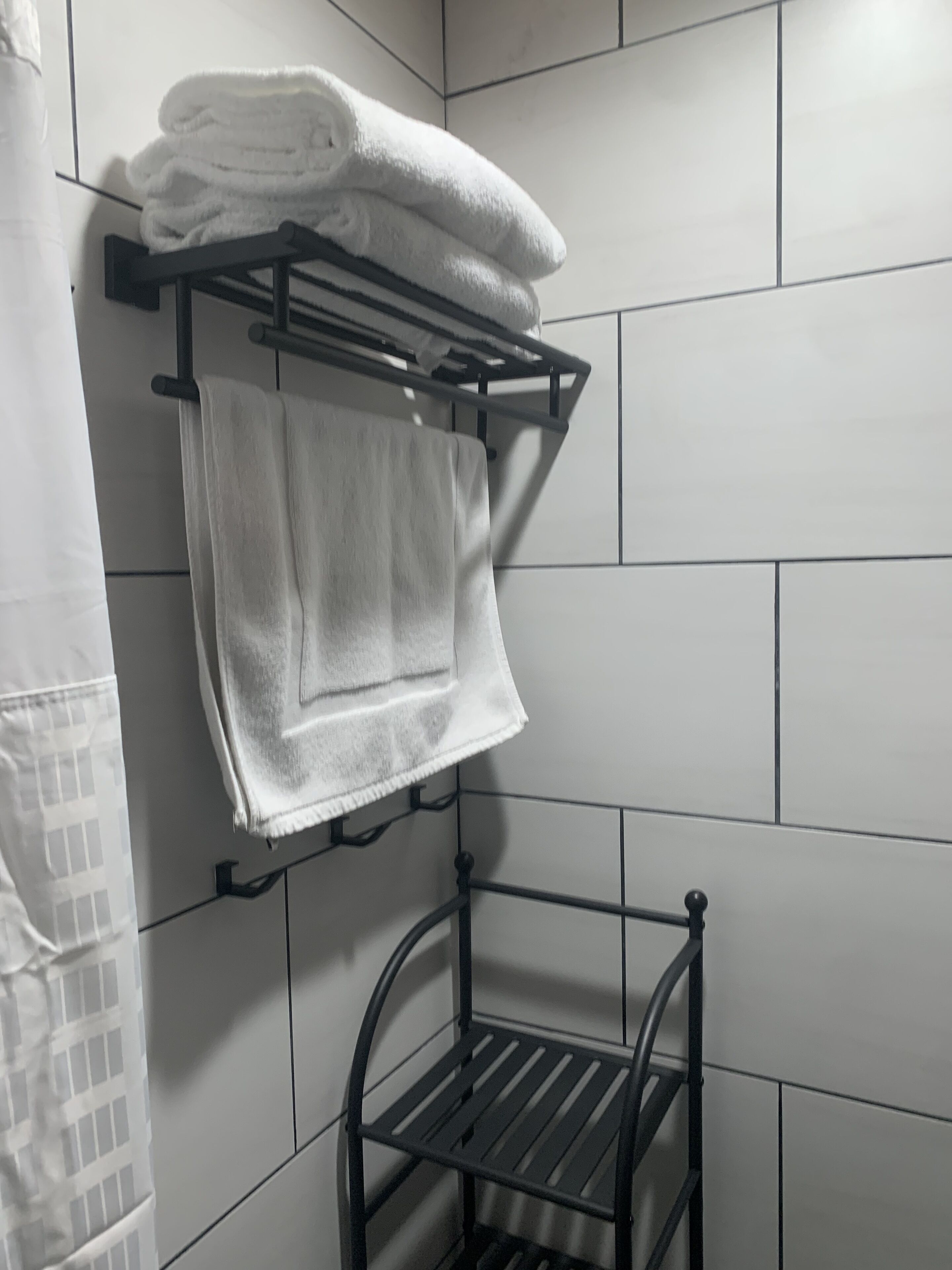 A bathroom with white tiled walls, a black towel rack holding folded towels, and a metal shelf unit.