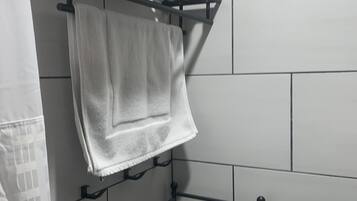 A bathroom with white tiled walls, a black towel rack holding folded towels, and a metal shelf unit.