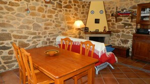 A stone-walled room with a wooden dining table, chairs, and a fireplace. - Little house with seaviews (Pedrafigueira)