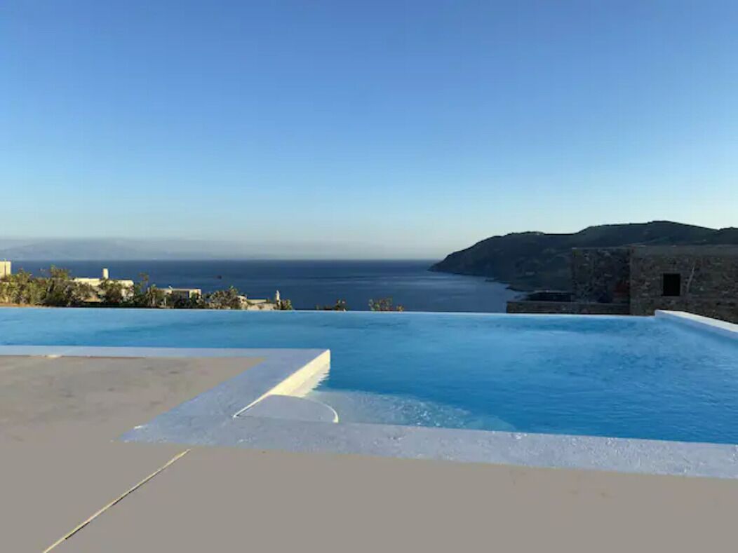 A swimming pool with a view of the sea and distant hills.