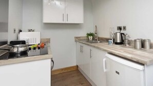 A modern kitchen with white cabinets, a built-in stove, and a countertop with a coffee maker and utensils. - Upper Calffield Farm (Haverfordwest)