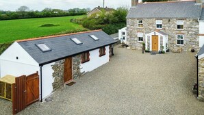 A stone house with a sloped roof and a white exterior, a gravel driveway, and a green field in the background. - Upper Calffield Farm (Haverfordwest)
