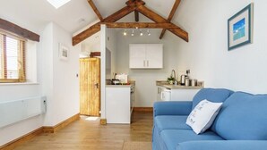 A modern kitchen with white cabinets, a blue sofa, and wooden beams on the ceiling. - Upper Calffield Farm (Haverfordwest)