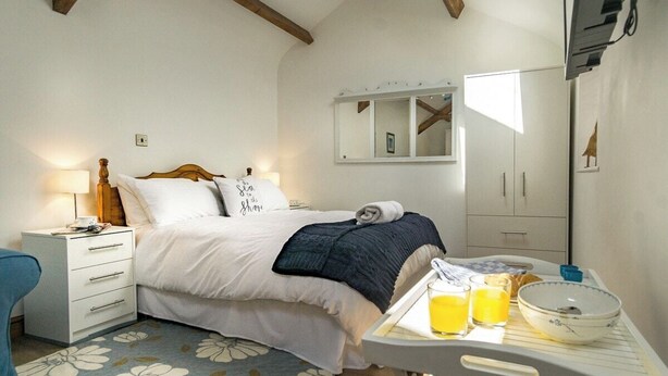 A bedroom with a bed, bedside table, and a breakfast tray with orange juice. - Upper Calffield Farm (Haverfordwest)