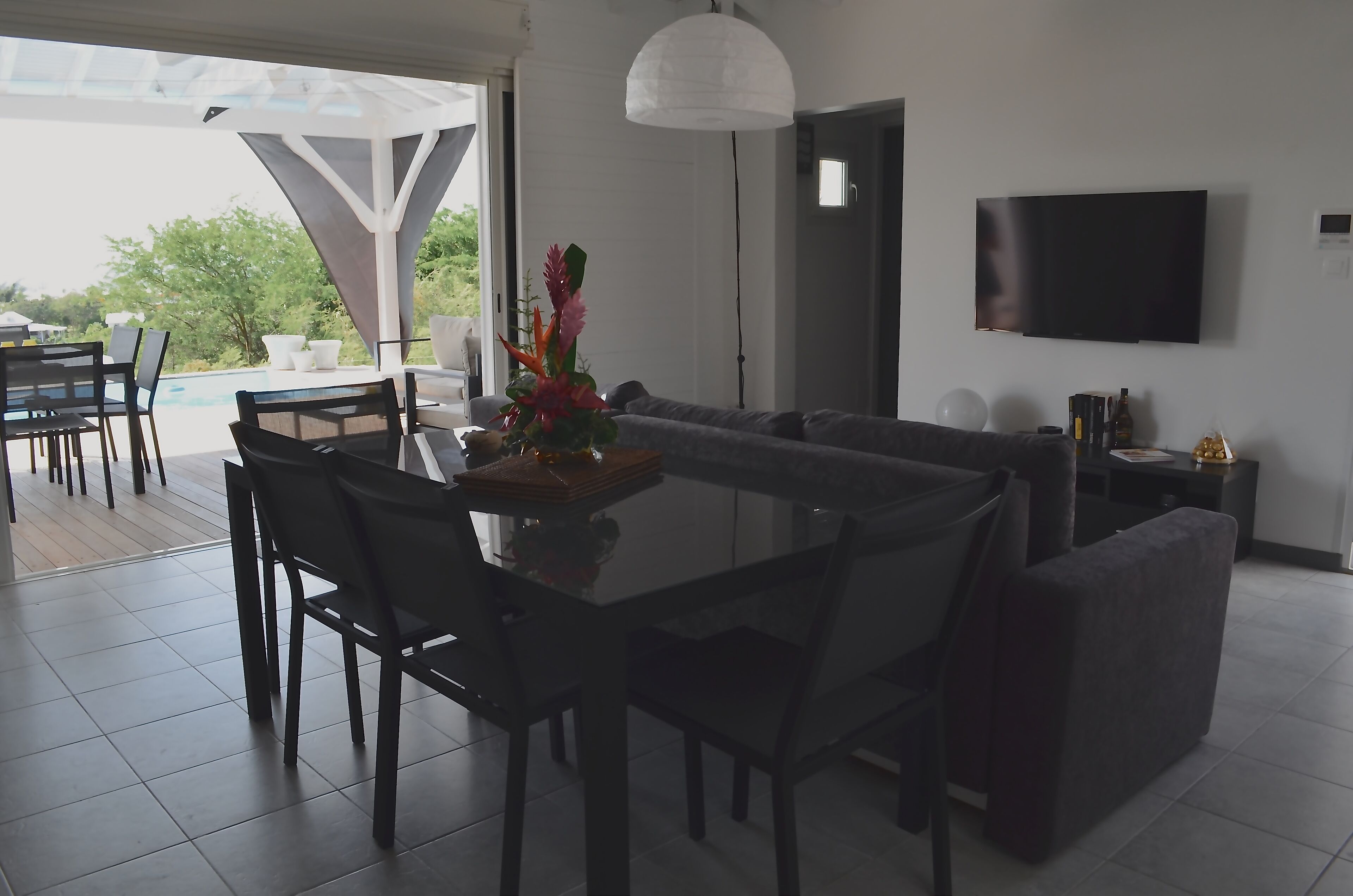 Moderni olohuone, jossa on lasinen ruokapöytä, tummat sohvat ja litteänäyttöinen televisio.