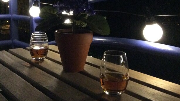 Ett träbord med två glas fyllda med en bärnstensfärgad vätska och en krukväxt med lila blommor.