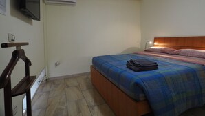A bedroom with a bed, a wooden headboard, a flat-screen TV mounted on the wall, an air conditioner, and a bedside table with a lamp. - in the beating heart of Naples, Italy (Napoli)
