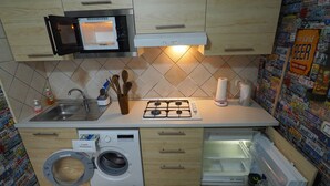 A compact kitchen with a microwave, stove, sink, and a washing machine. - in the beating heart of Naples, Italy (Napoli)