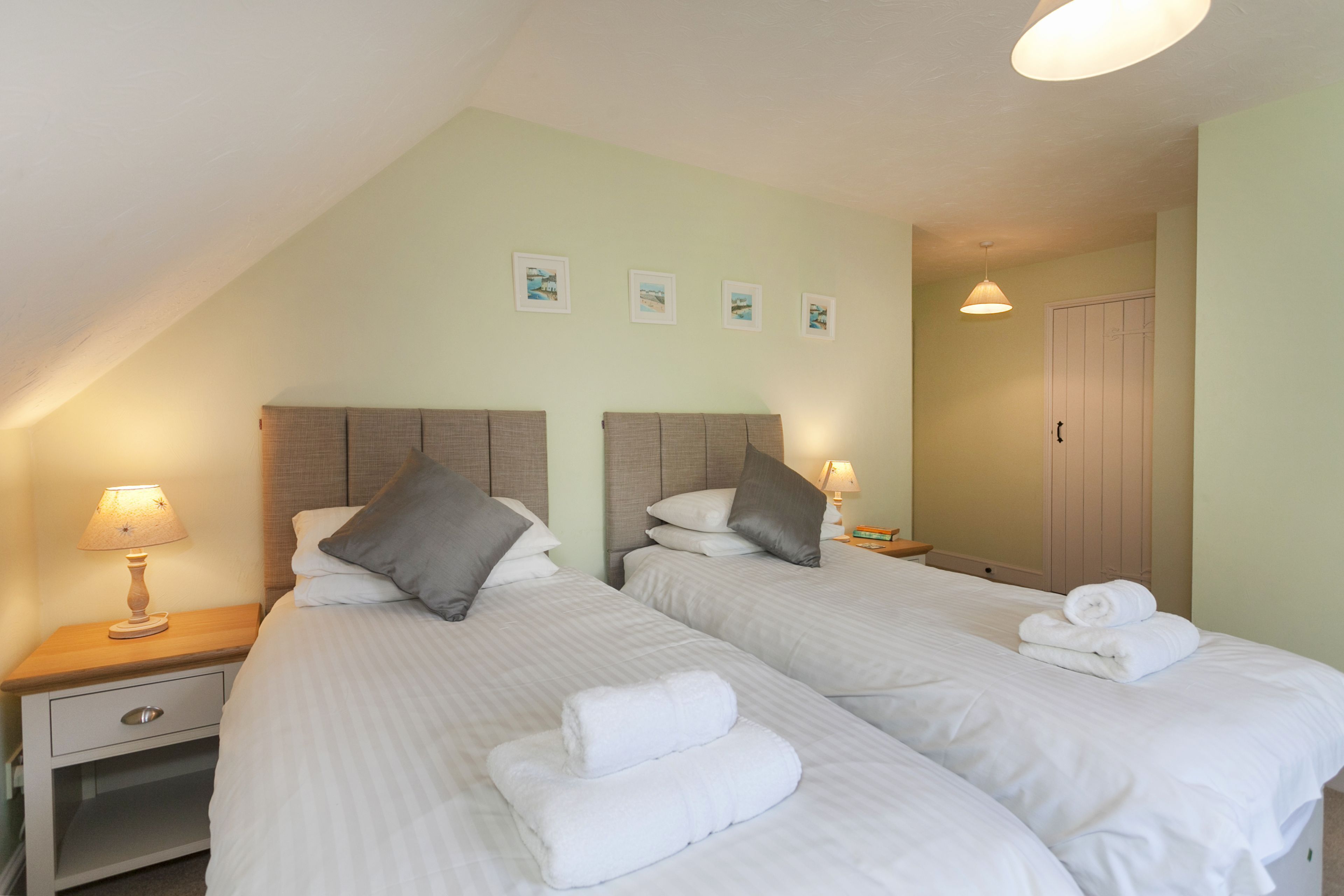 A hotel room with two beds, each with a headboard, bedside tables with lamps, and a door with a handle.