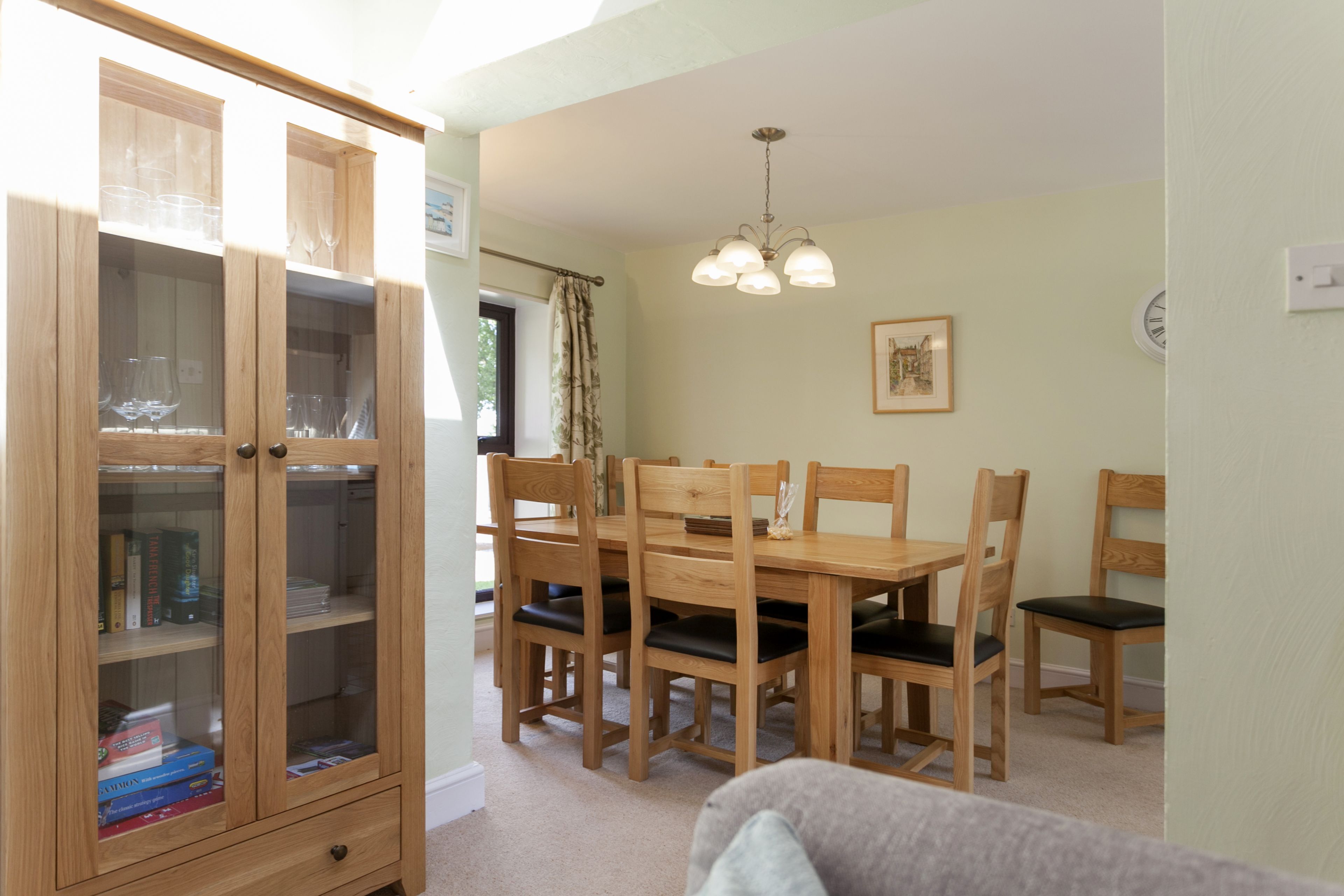 A dining area with a wooden table and chairs, a glass-fronted cabinet, and a chandelier.