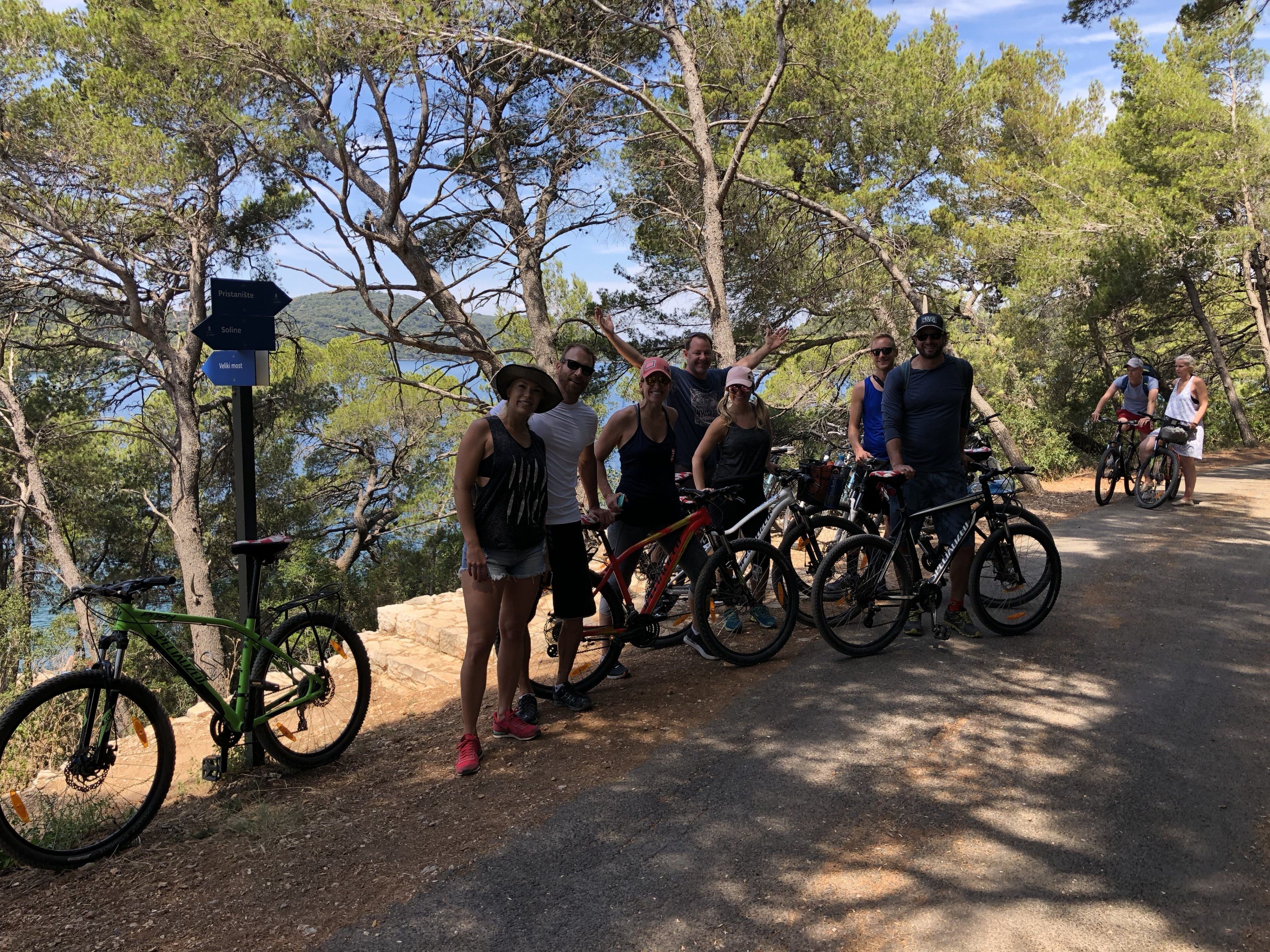 A group of people standing by bicycles on a paved path surrounded by trees.
