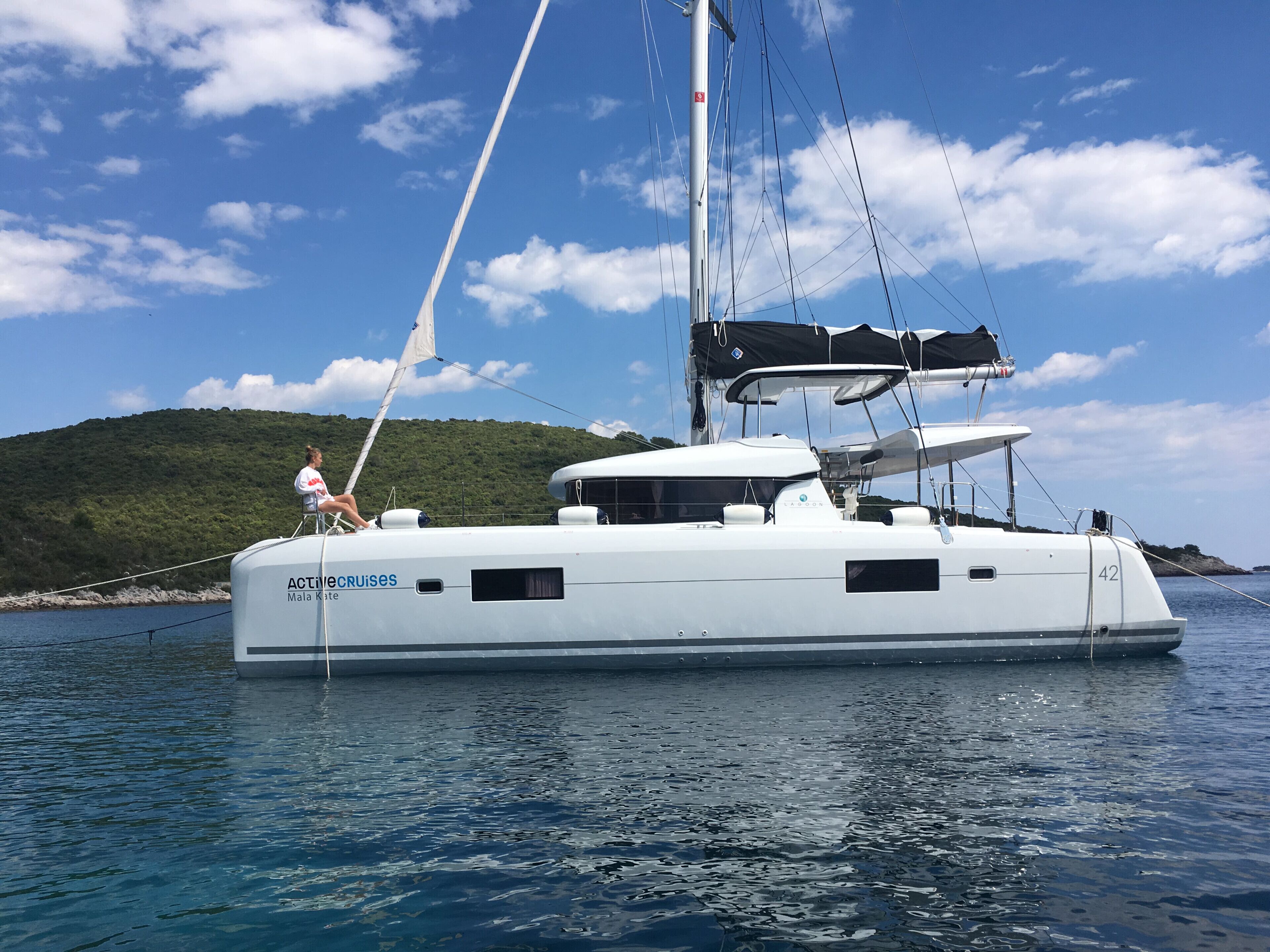 Un yacht blanc avec une personne sur le pont, un mât et une cabine dotée de fenêtres.