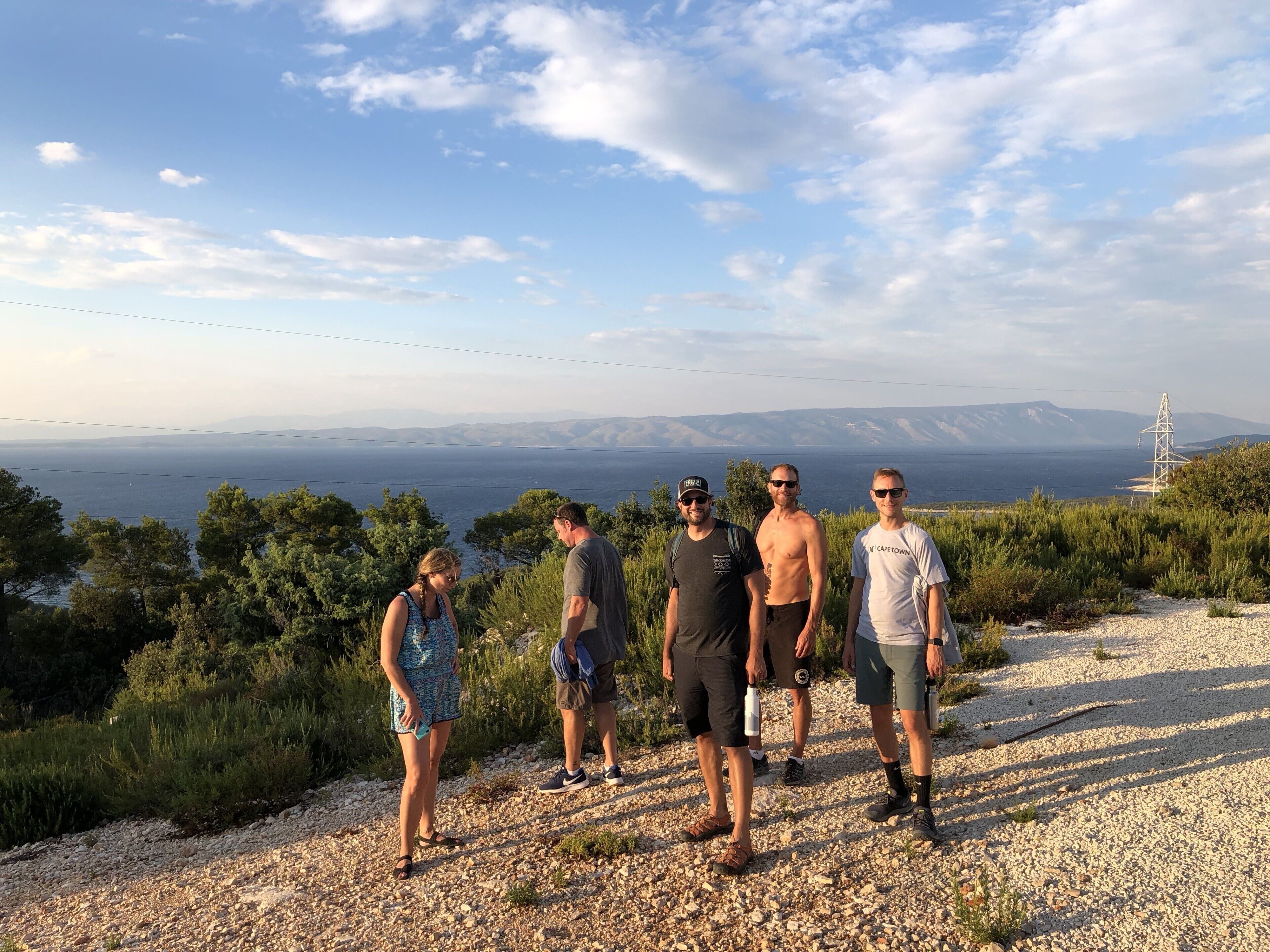 En grupp människor står på en grusgång med en vacker utsikt över havet och bergen i bakgrunden.