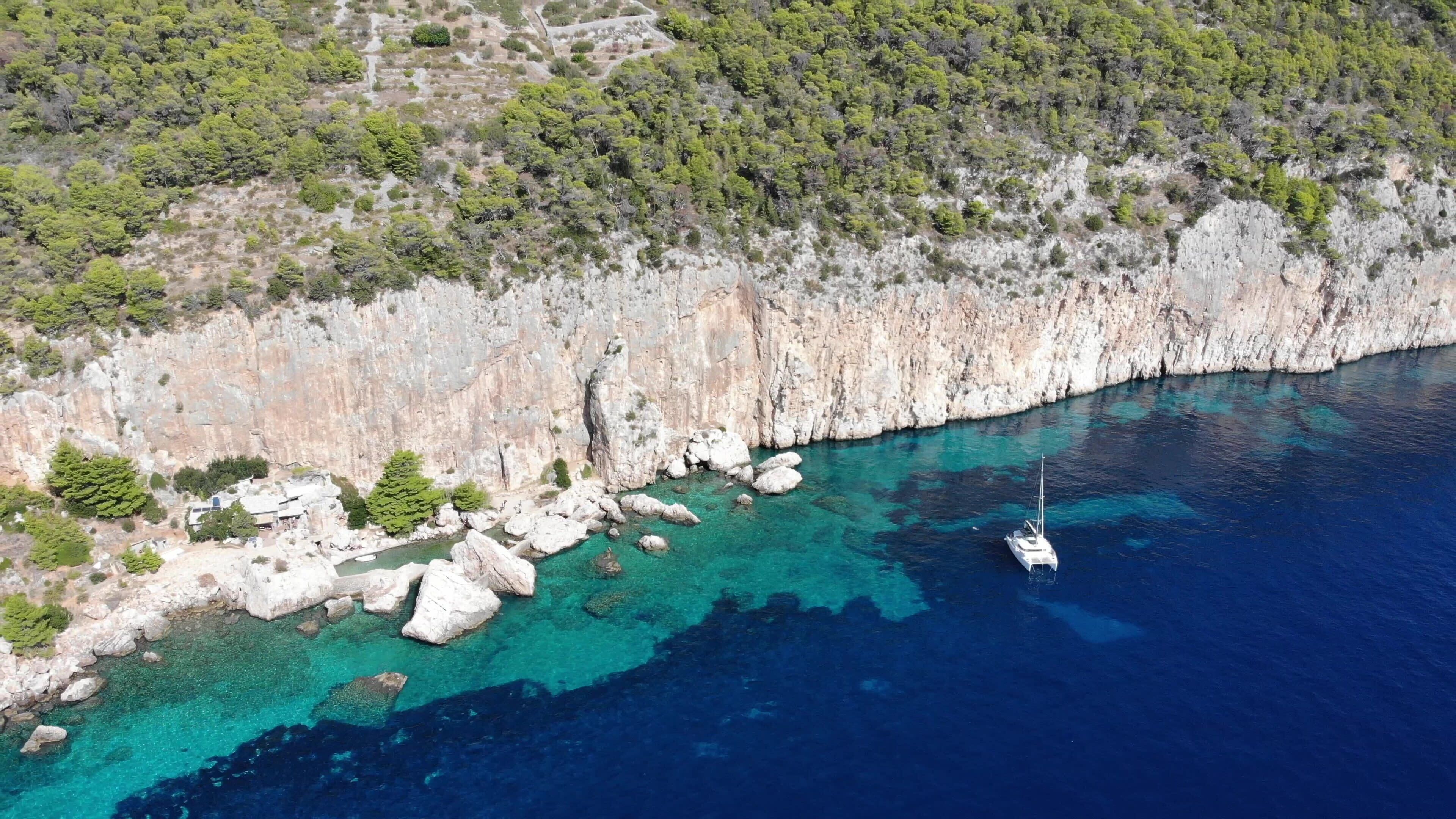 A coastal area with rocky cliffs, clear turquoise waters, and a sailboat anchored near the shore.