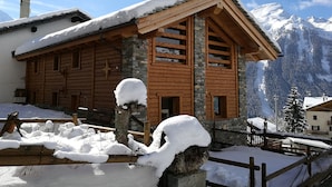 Una cabaña de madera con detalles de piedra, rodeada de montañas nevadas.