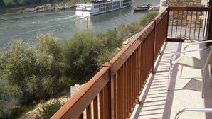 Un balcón con vistas a un río, una embarcación y colinas circundantes.