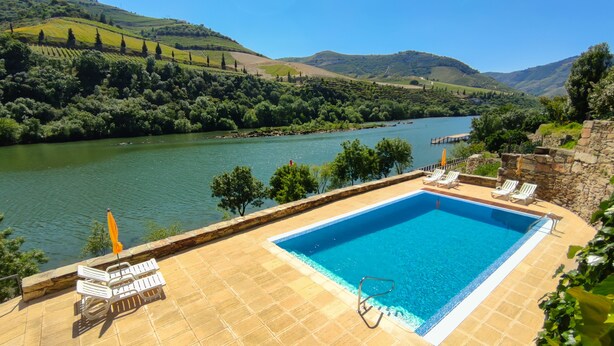 Piscina rectangular con solárium de piedra, rodeada de sillas de descanso y un muro de piedra.
