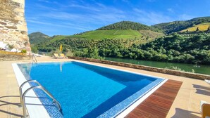 Una piscina con muelle de madera, pared de piedra y vistas a un río y colinas.