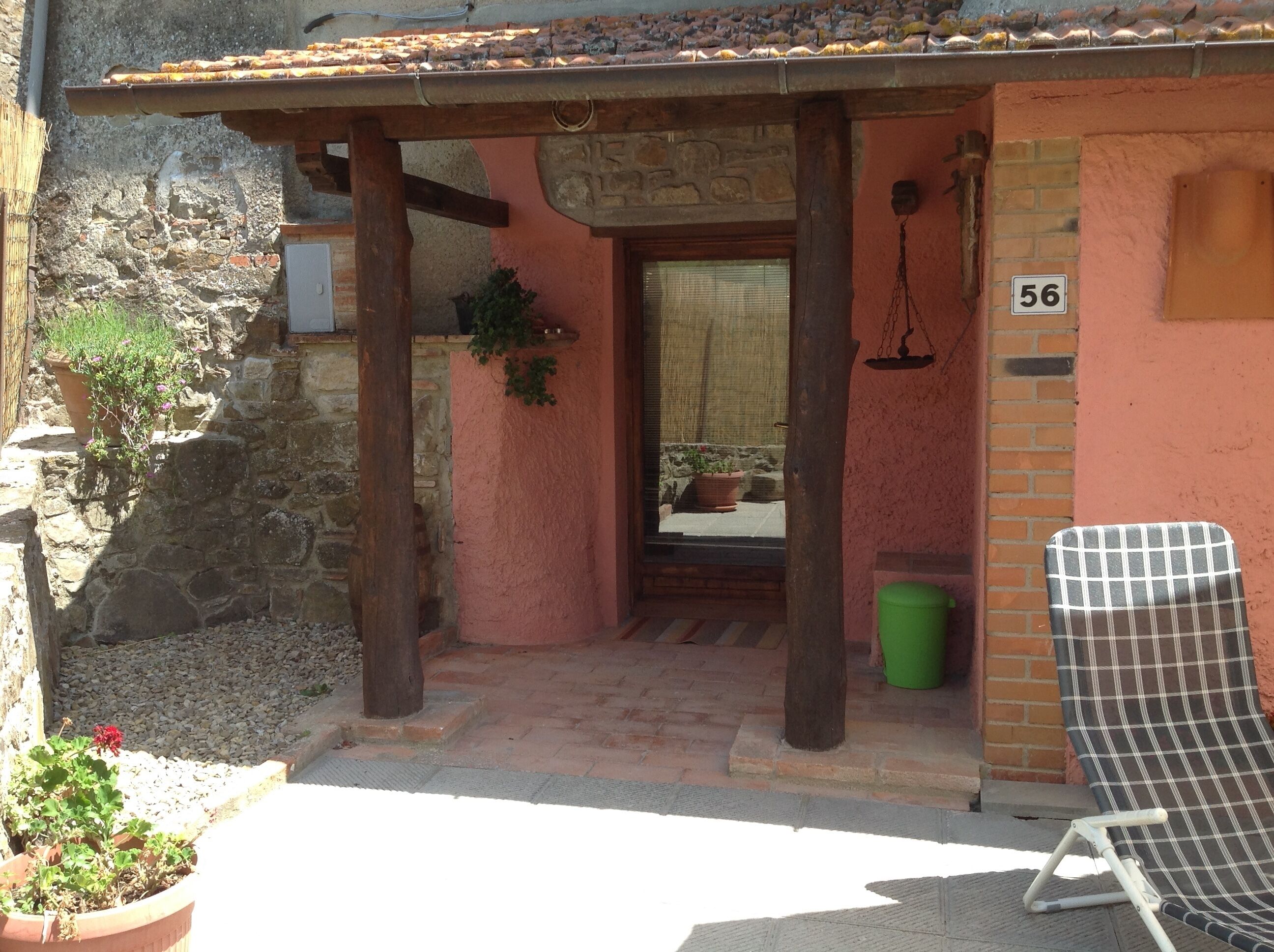 Une entrée rustique, avec un mur en pierre, une porte en bois et un balcon agrémenté d’une chaise à motifs à carreaux.